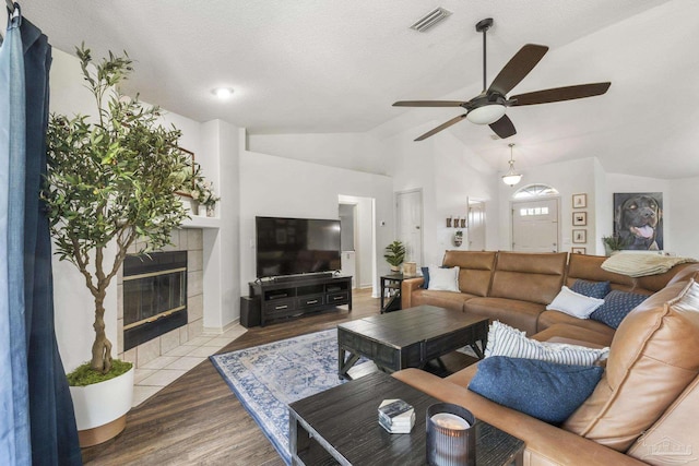 living room with hardwood / wood-style floors, lofted ceiling, a tile fireplace, ceiling fan, and a textured ceiling