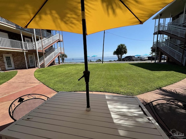 deck with a water view, a lawn, and stairway