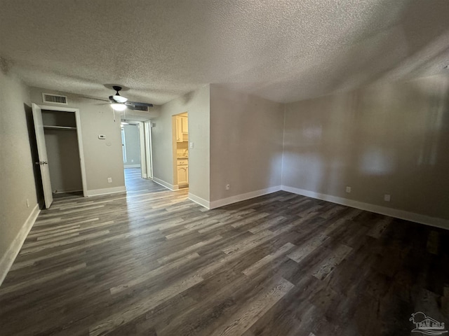 empty room featuring baseboards, visible vents, dark wood finished floors, and a textured ceiling