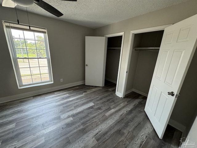 unfurnished bedroom with baseboards, a ceiling fan, dark wood-style floors, a textured ceiling, and multiple closets