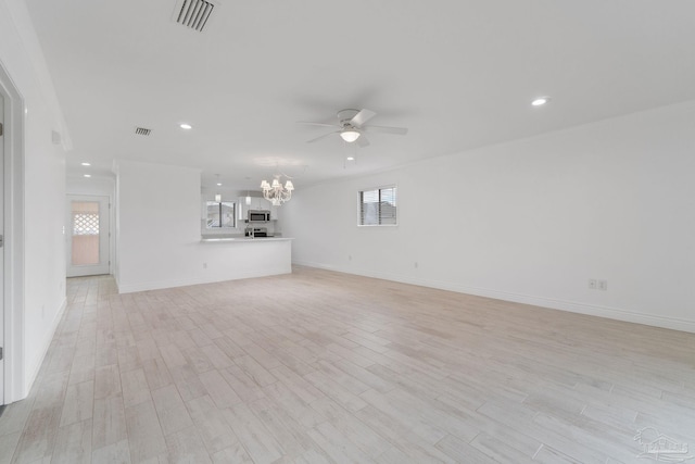 unfurnished living room with a wealth of natural light, visible vents, ceiling fan with notable chandelier, and light wood-type flooring