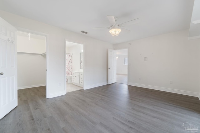 unfurnished bedroom with visible vents, a ceiling fan, wood finished floors, baseboards, and a spacious closet