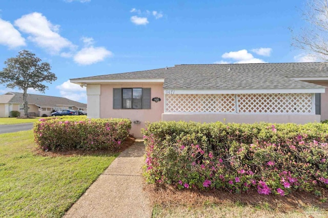 view of front of property with stucco siding, a front yard, and a shingled roof