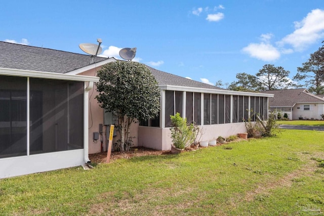 back of house with stucco siding, a lawn, roof with shingles, and a sunroom