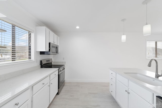 kitchen featuring hanging light fixtures, appliances with stainless steel finishes, white cabinetry, and a sink