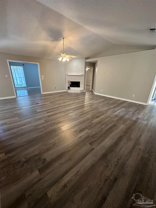 unfurnished living room featuring a textured ceiling, dark hardwood / wood-style floors, a tiled fireplace, lofted ceiling, and ceiling fan