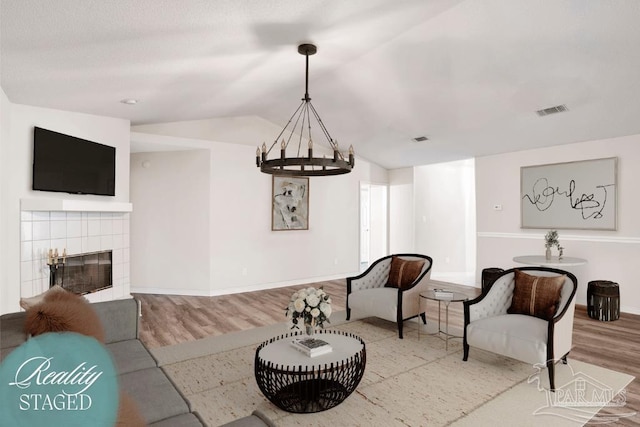 living area featuring visible vents, baseboards, vaulted ceiling, an inviting chandelier, and wood finished floors