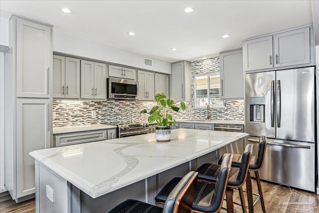 342 Ft Pickens Rd, Pensacola Beach, FL 32561 - kitchen featuring appliances with stainless steel finishes, gray cabinetry, backsplash, dark wood-type flooring, and a breakfast bar