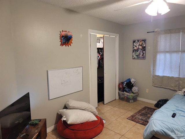 bedroom with baseboards, ceiling fan, a textured ceiling, a closet, and light tile patterned flooring