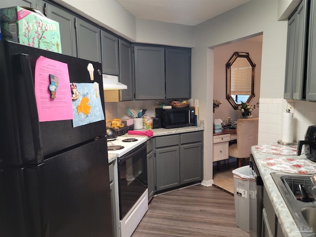 kitchen featuring gray cabinets, light countertops, decorative backsplash, under cabinet range hood, and black appliances