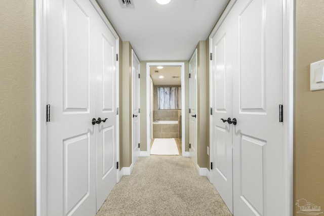 corridor featuring light carpet, visible vents, and baseboards