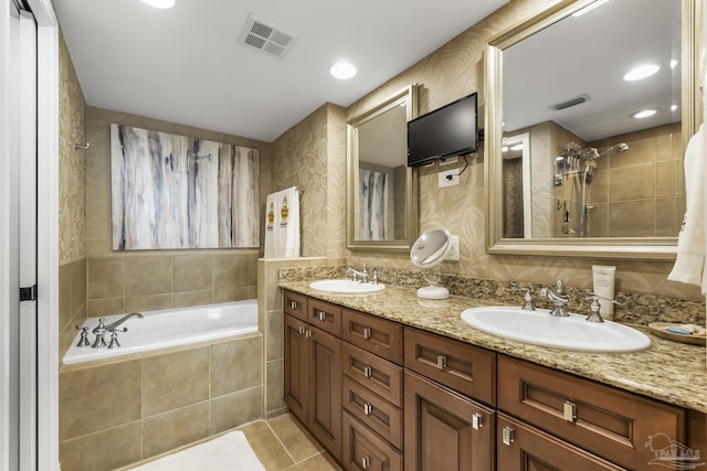 full bathroom featuring tiled bath, visible vents, and a sink