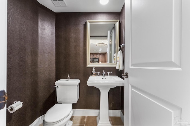 half bathroom with tile patterned flooring, toilet, a sink, visible vents, and baseboards