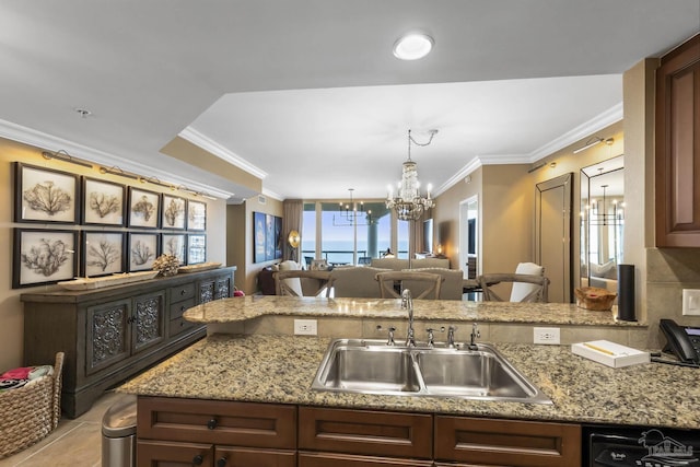 kitchen with a notable chandelier, a sink, open floor plan, light stone countertops, and crown molding