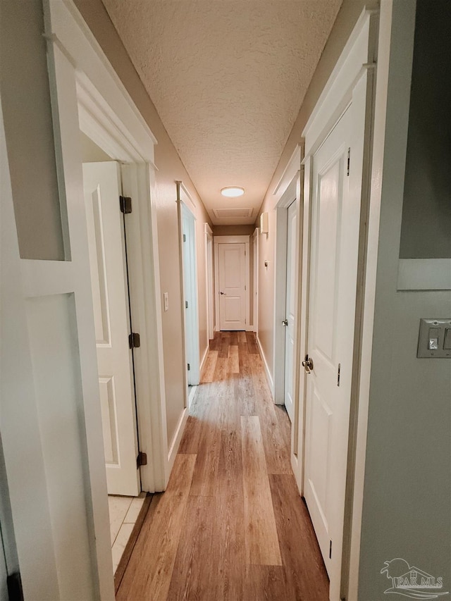 corridor featuring a textured ceiling and light hardwood / wood-style floors