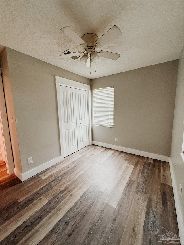 unfurnished bedroom featuring wood-type flooring, a textured ceiling, a closet, and ceiling fan