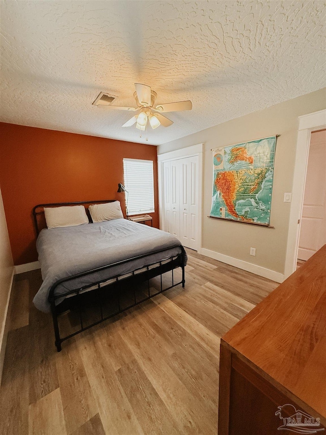 bedroom with ceiling fan, a closet, light hardwood / wood-style floors, and a textured ceiling