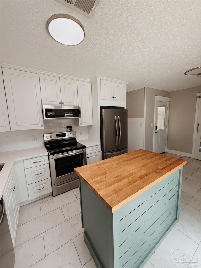 kitchen featuring white cabinets, a center island, appliances with stainless steel finishes, and wooden counters