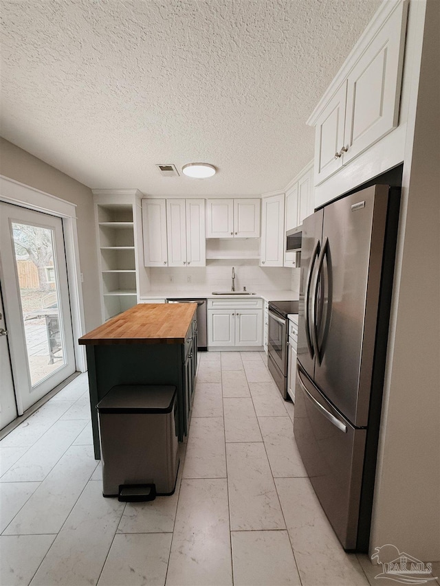 kitchen with white cabinets, sink, a kitchen island, butcher block counters, and stainless steel appliances