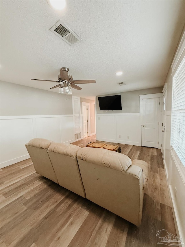 living room with a wealth of natural light, light hardwood / wood-style flooring, ceiling fan, and a textured ceiling