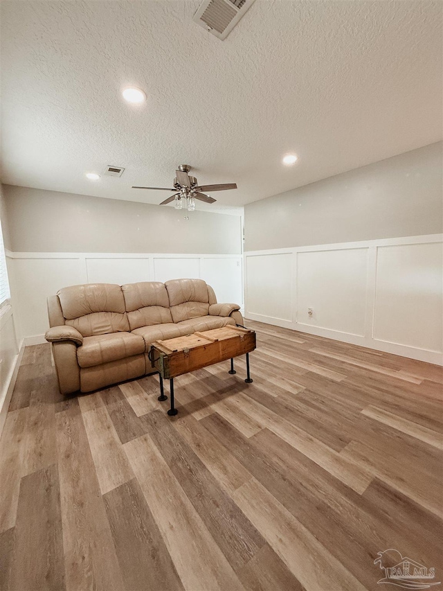 living room featuring ceiling fan, light hardwood / wood-style floors, and a textured ceiling