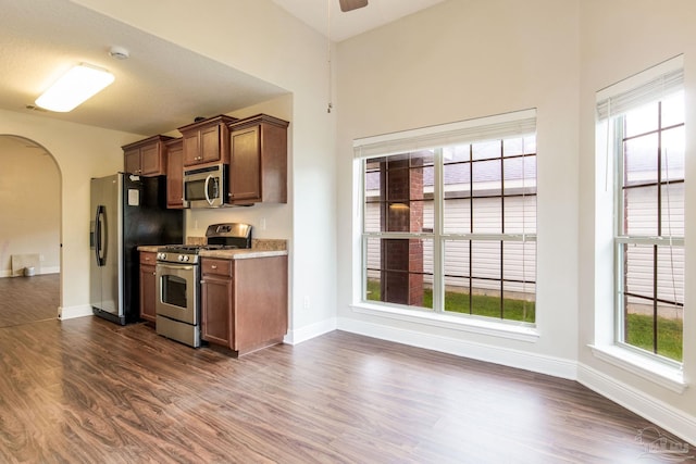 kitchen featuring baseboards, arched walkways, a ceiling fan, stainless steel appliances, and dark wood-type flooring