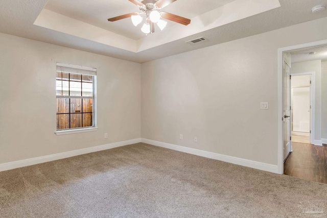 carpeted empty room with visible vents, ceiling fan, baseboards, and a raised ceiling