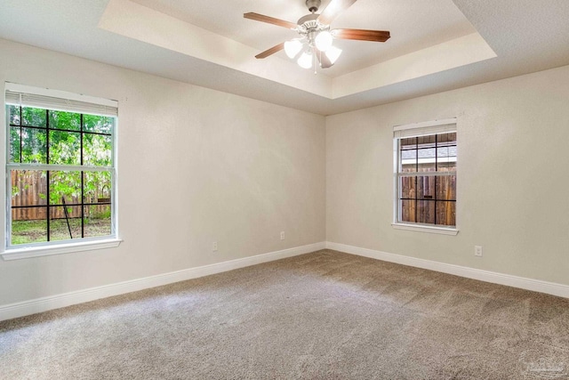 spare room with a tray ceiling, baseboards, a ceiling fan, and carpet