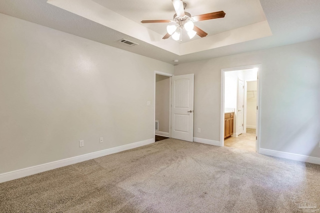 empty room with baseboards, visible vents, a tray ceiling, ceiling fan, and light colored carpet
