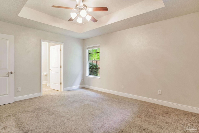 empty room with light colored carpet, baseboards, a ceiling fan, and a raised ceiling