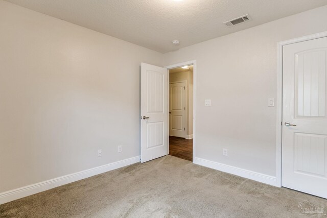 unfurnished room featuring visible vents, baseboards, light carpet, and a textured ceiling