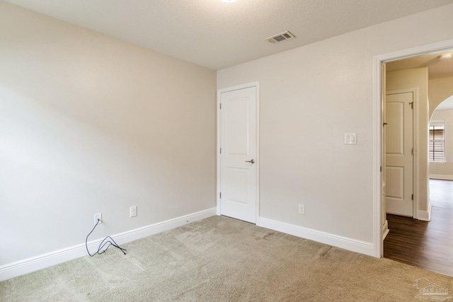 carpeted empty room with visible vents, baseboards, arched walkways, and a textured ceiling