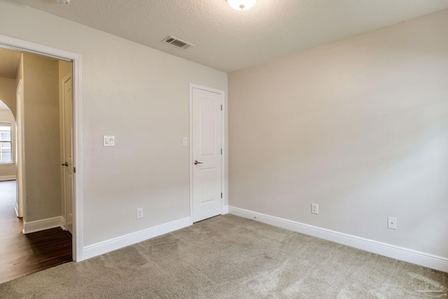 spare room featuring visible vents, baseboards, arched walkways, a textured ceiling, and carpet floors