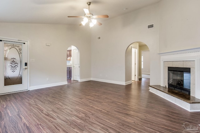 unfurnished living room with dark wood-type flooring, visible vents, ceiling fan, and arched walkways