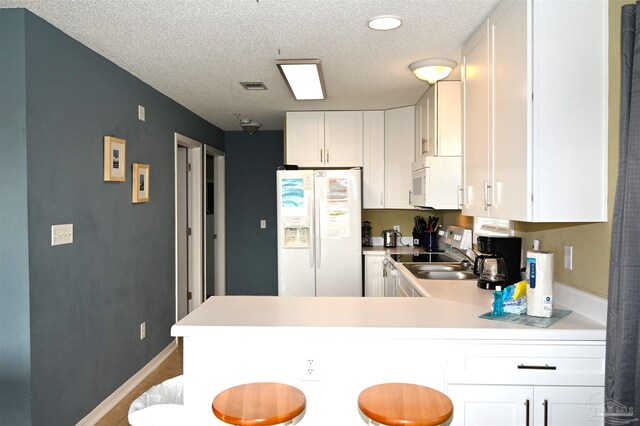 kitchen featuring white cabinetry, a textured ceiling, white appliances, and kitchen peninsula