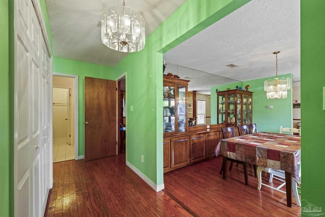 dining room featuring dark wood-type flooring, a textured ceiling, and an inviting chandelier