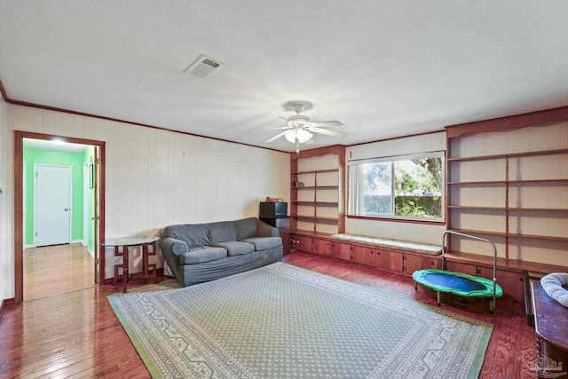 living room featuring ornamental molding, dark wood-type flooring, ceiling fan, and a textured ceiling