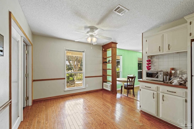 kitchen with white cabinetry, ceiling fan, light hardwood / wood-style flooring, and backsplash