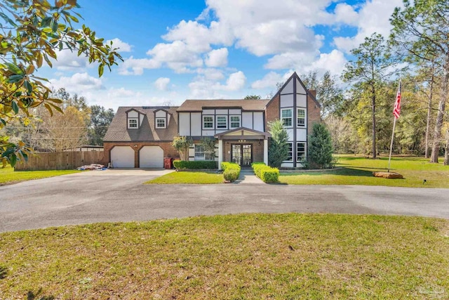 english style home featuring fence, aphalt driveway, a front yard, french doors, and a garage