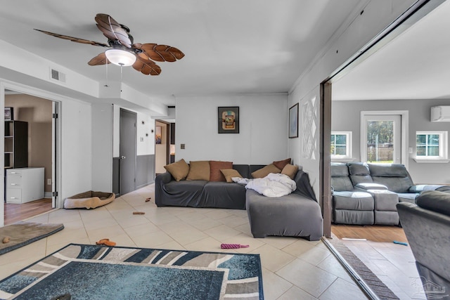 living area featuring a wall unit AC, light tile patterned floors, visible vents, and ceiling fan