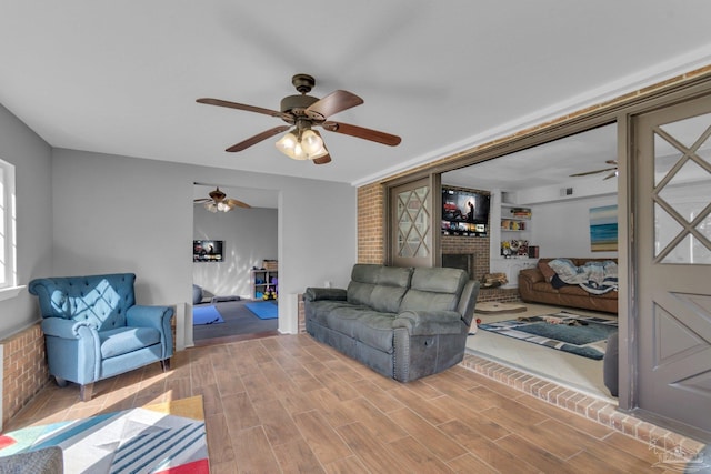 living room featuring a brick fireplace, a ceiling fan, and wood finish floors