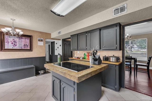 kitchen with light tile patterned flooring, a notable chandelier, black electric cooktop, and a wainscoted wall