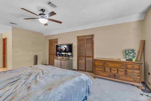 carpeted bedroom featuring two closets, visible vents, a textured ceiling, and a ceiling fan