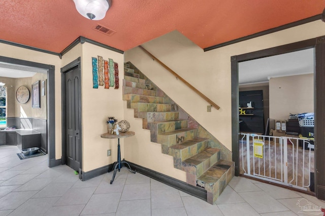 staircase with tile patterned flooring, a textured ceiling, visible vents, and ornamental molding