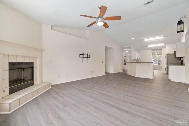 unfurnished living room with light hardwood / wood-style flooring, a tile fireplace, ceiling fan, and vaulted ceiling