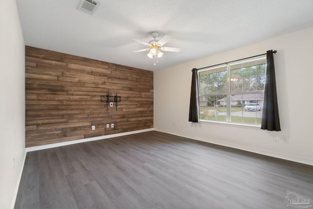 spare room with dark hardwood / wood-style flooring, ceiling fan, a textured ceiling, and wooden walls