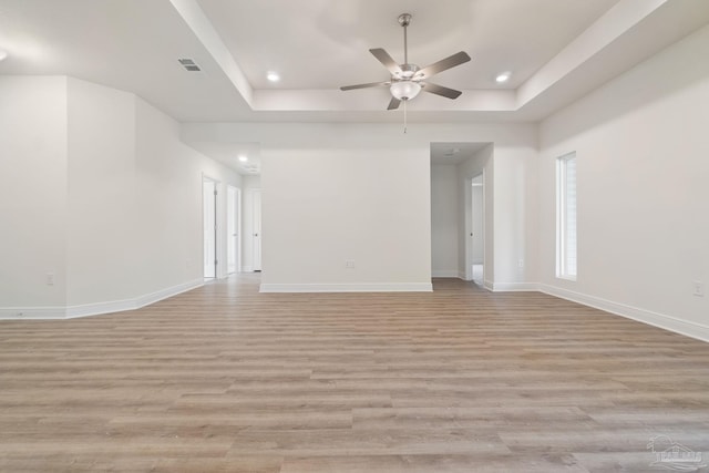 spare room with a raised ceiling, ceiling fan, and light wood-type flooring