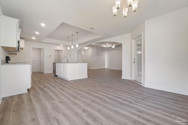 kitchen featuring hanging light fixtures, ceiling fan with notable chandelier, light hardwood / wood-style floors, white cabinetry, and a tray ceiling