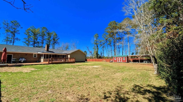 view of yard featuring a wooden deck, an outbuilding, a shed, and fence