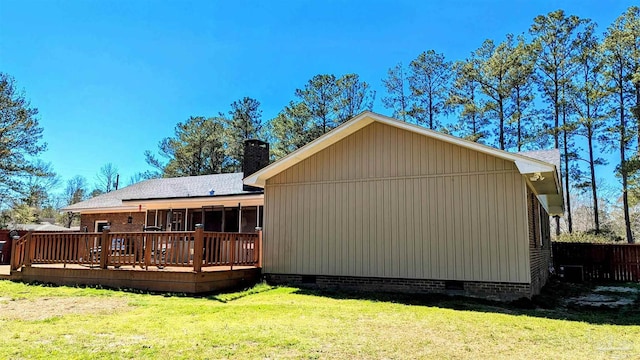 rear view of property featuring a wooden deck, a shingled roof, a chimney, crawl space, and a lawn